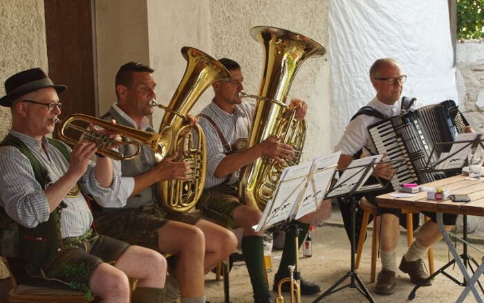 Die Musikanten der Wirtshausmuse sitzen beim Spielen unter einem Vordach